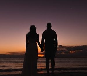 couple holding hands on a beach whilst watching the sunset