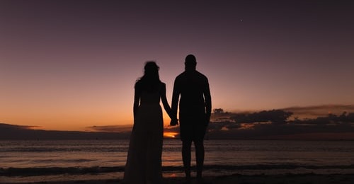 couple holding hands on a beach whilst watching the sunset