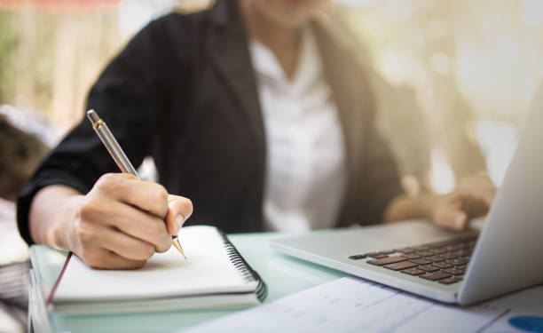 student in a public library making notes on a notebook using her laptop